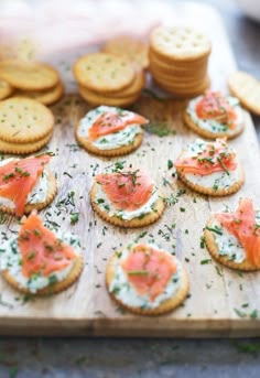 crackers topped with salmon and cream cheese on a wooden board next to crackers