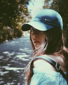 a woman wearing a blue hat standing on the side of a road with trees in the background