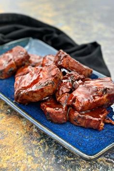 a blue plate topped with pieces of meat covered in sauce on top of a table