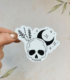 a person holding up a sticker with a skull and moon design on the side