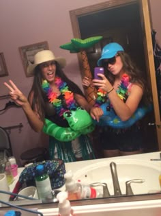 two women dressed in costumes are taking a selfie with their cell phones as they stand in front of a bathroom mirror