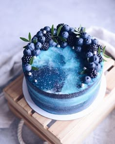 a cake with blue icing and berries on top is sitting on a wooden tray