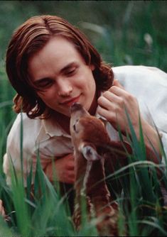 a young man is holding a baby deer in the tall grass and looking at it