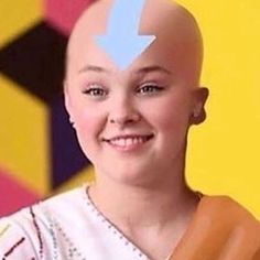 a woman with a shaved head and blue arrows painted on her forehead smiles at the camera