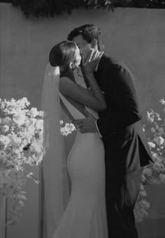 a bride and groom kissing in front of white flowers at their wedding ceremony, black and white photograph