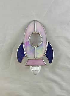 a space shuttle shaped glass night light on a white surface with a blue, pink and purple stripe around it