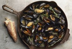 a pan filled with mussels on top of a table next to a piece of bread