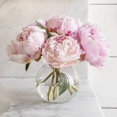 pink peonies in a clear vase on a marble table