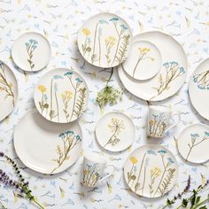 a table topped with lots of white plates covered in wildflowers and plants next to each other