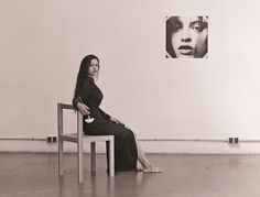 a woman sitting on top of a wooden chair next to a wall with pictures above her