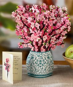 a vase filled with pink flowers next to an apple and greeting card on a table