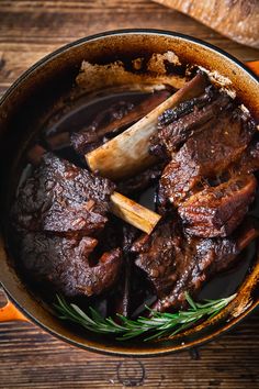 a pot filled with beef and carrots on top of a wooden table next to bread