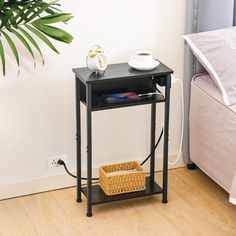 a small black table with a basket on it next to a bed and a plant