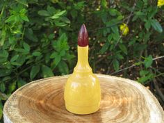 a small yellow vase sitting on top of a tree stump