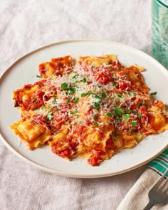 a white plate topped with pasta covered in sauce and parmesan cheese next to a glass of water