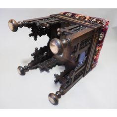 an intricately designed wooden box with metal knobs and wheels on the front, sitting on a white surface