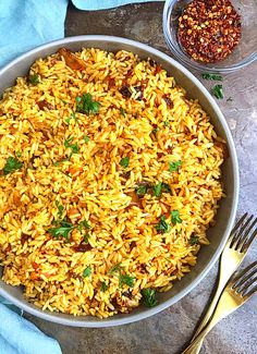 a bowl filled with yellow rice next to some silverware