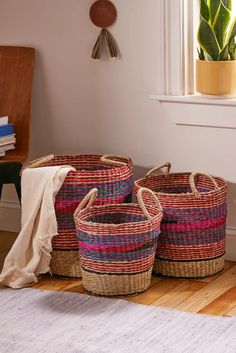 three woven baskets sitting on top of a wooden floor next to a potted plant