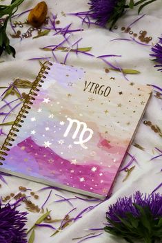 a notebook with the word virgo written on it and purple flowers scattered around it