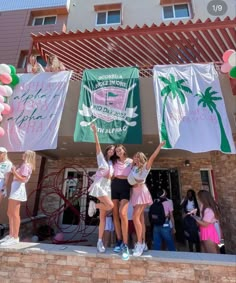 some girls are holding up signs and balloons in front of a building with palm trees