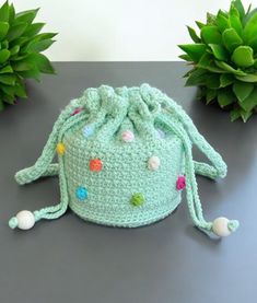 a green crocheted bag sitting on top of a table next to potted plants