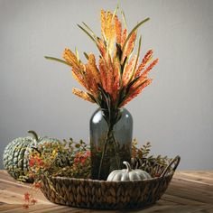 an arrangement of flowers and pumpkins in a vase on a wooden table with other autumn decorations