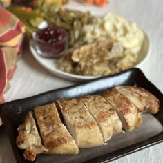 some meat is sitting on a black plate and next to mashed potatoes, as well as other food