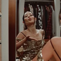 a woman in a gold dress looking at herself in the mirror and making a face