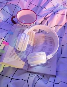 an open book with headphones on top of it next to a cup of coffee