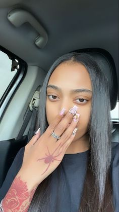 a woman with long grey hair sitting in a car holding her hand to her face