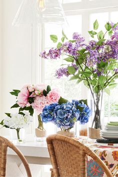 a dining room table with flowers in vases and plates on the placemates