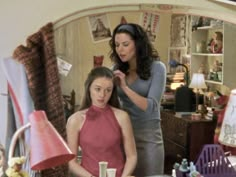 a woman is getting her hair styled by another woman in a room with other items