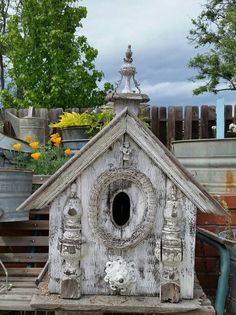 a birdhouse made out of wood with flowers in the back ground and an old tin canister behind it