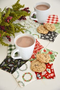 two mugs of hot chocolate and cookies are sitting on the table next to christmas napkins