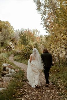 a bride and groom walking down a path in the woods