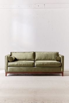 a green leather couch sitting on top of a white floor next to a wooden frame