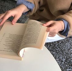 a person sitting at a table reading a book with their hands on top of the book