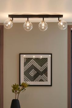 three lights are hanging above a table with a vase on it and a plant in the foreground