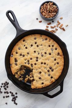 a chocolate chip cookie in a cast iron skillet next to pecans and nuts