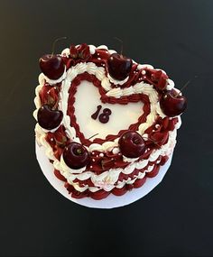 a heart - shaped cake with cherries on top sits on a black surface, ready to be eaten