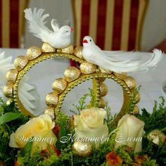 two white doves sitting on top of a table surrounded by flowers and greenery