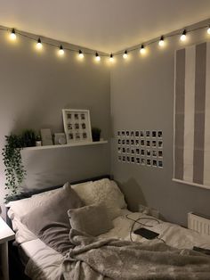 an unmade bed in a bedroom with string lights on the wall and pictures hanging above it