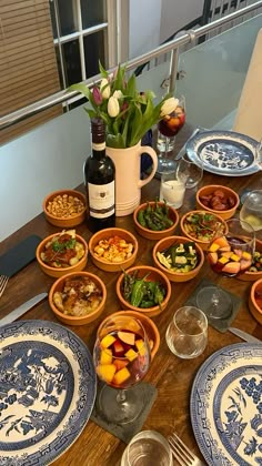 a wooden table topped with blue and white dishes filled with food next to a bottle of wine