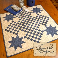 a quilted table runner with blue and white stars on it next to a book