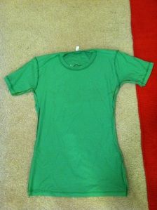 a green t - shirt laying on the floor next to a red and white towel