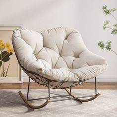 a white rocking chair sitting on top of a rug next to a vase with yellow flowers