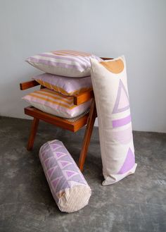 three pillows stacked on top of each other next to a wooden chair with a pillow