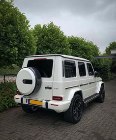 a white mercedes g - class is parked in front of some bushes