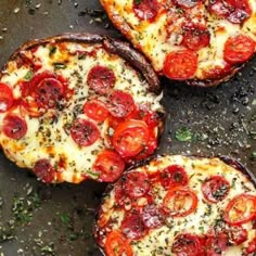 three small pizzas with tomatoes and cheese on them sitting on a baking sheet, ready to be eaten