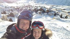 a man and woman taking a selfie on the top of a ski slope with snow covered mountains in the background